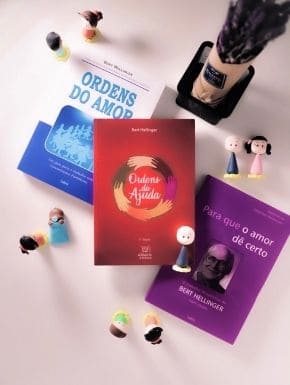 Fotografia com três livros escritos por Bert Hellinger, vários bonequinhos de biscuit e um arranjo de flores de lavanda embrulhadas em papel pardo